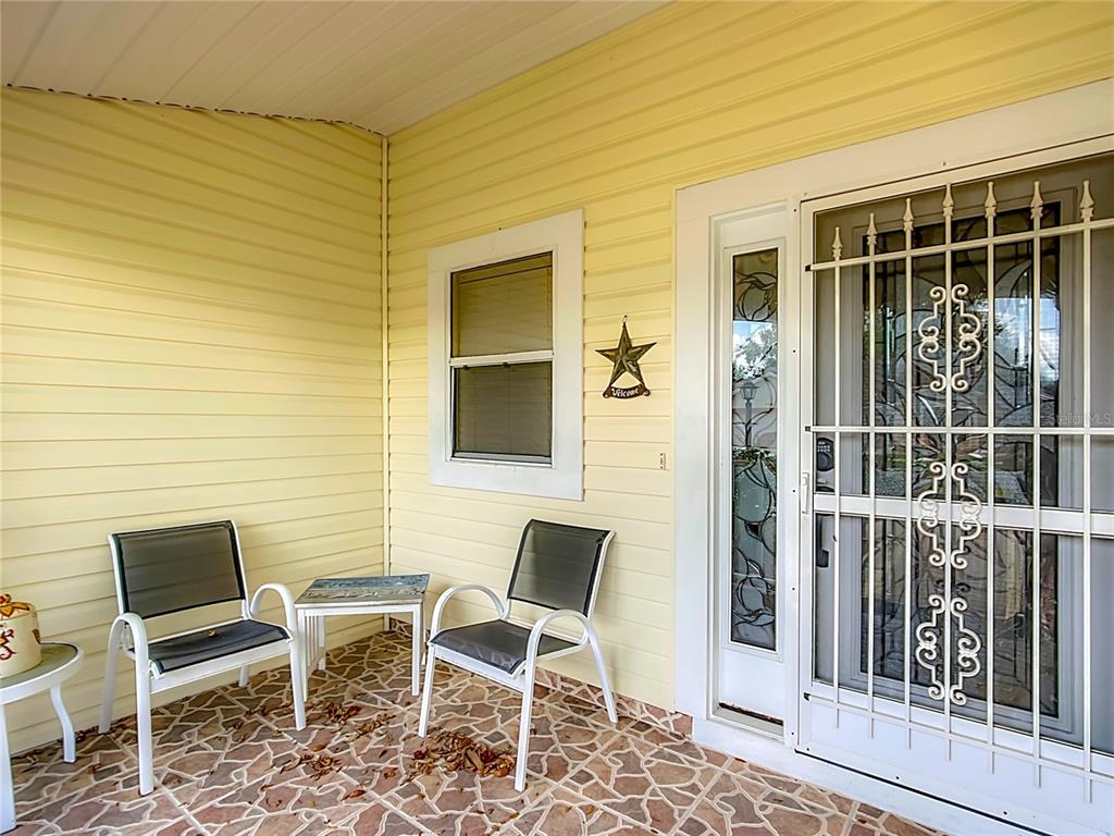 A covered front porch features yellow siding, two chairs, a small table, and a security door — 208 DESOTA COURT, LADY LAKE, FL