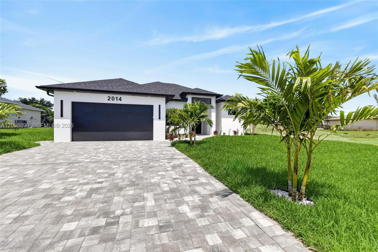 A modern single-story house features a dark garage door, white exterior, and paved driveway — 2014 SW 8th PL, Cape Coral FL 33991, CAPE CORAL, FL