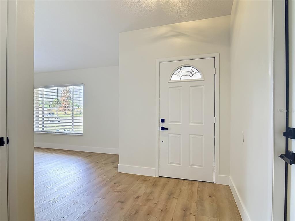 An entryway with light wood-look flooring, white walls, and a white front door — 921 FORT SMITH BOULEVARD, DELTONA, FL