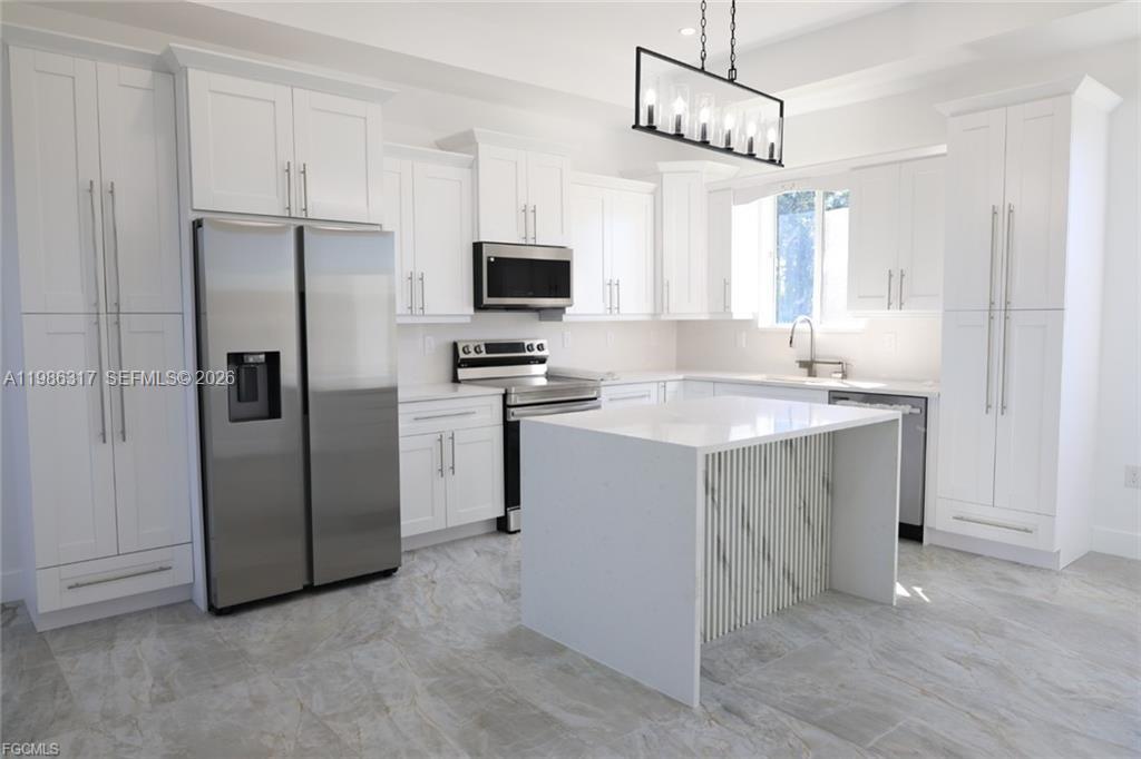 A modern kitchen features white cabinetry, stainless steel appliances, and a white marble-patterned island — 114 PRESTON ST, Lehigh Acres FL 33974, LEHIGH ACRES, FL