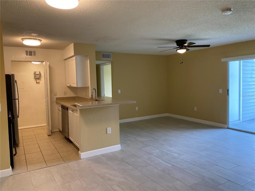 An open-concept kitchen with white cabinets and a breakfast bar overlooks a tiled living area — 1225 BERMUDA LAKES LANE UNIT 107, KISSIMMEE, FL
