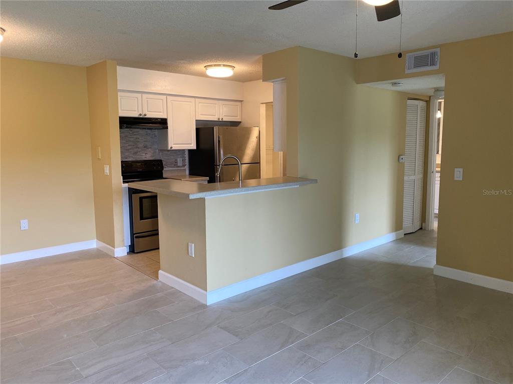 A kitchen with white cabinets and stainless steel appliances overlooks a tiled living area — 1225 BERMUDA LAKES LANE UNIT 107, KISSIMMEE, FL