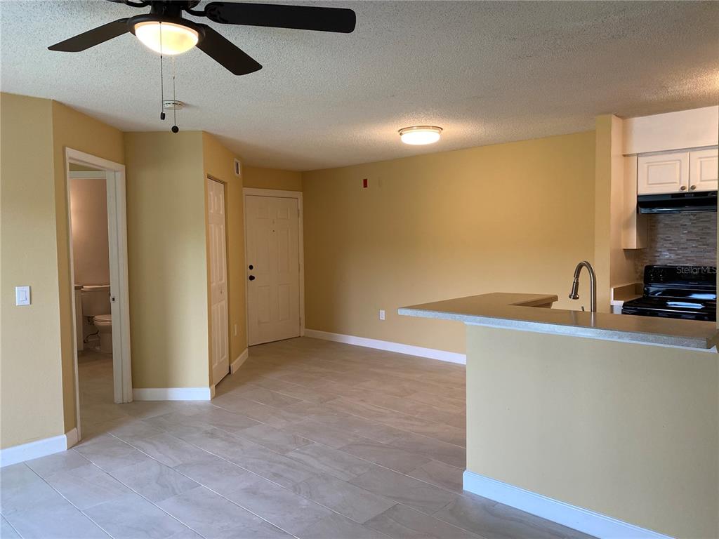 An open-concept living area features light-colored tile flooring, yellow walls, and a kitchen breakfast bar — 1225 BERMUDA LAKES LANE UNIT 107, KISSIMMEE, FL
