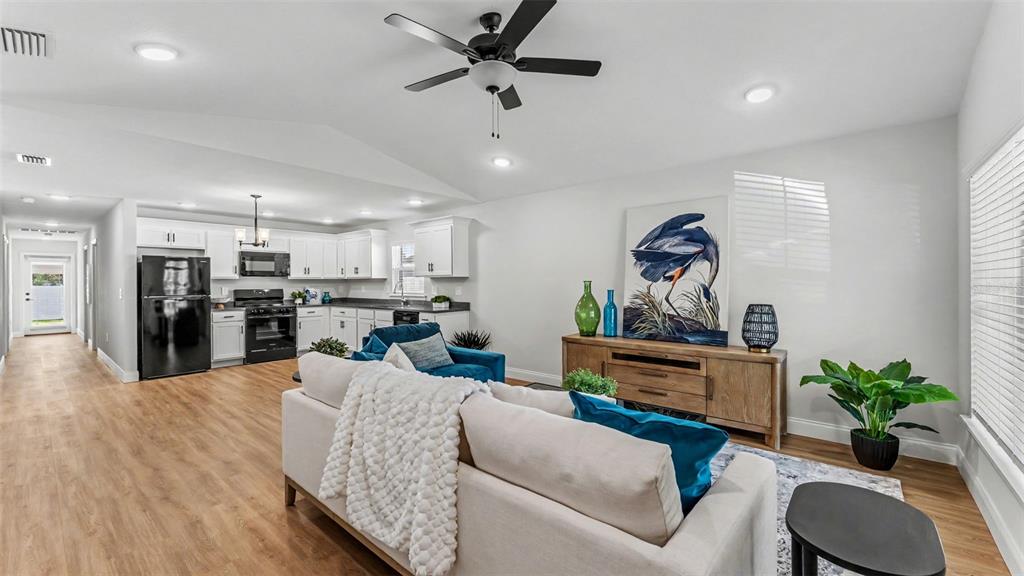 An open-concept living room and kitchen feature light wood flooring, white cabinetry, and vaulted ceilings — 1242 DOROTHY STREET, LAKELAND, FL