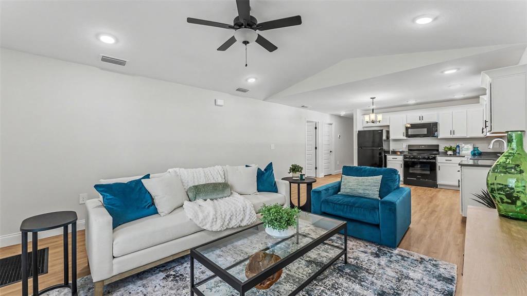 A living room with a white sofa, blue armchair, glass coffee table, and open kitchen — 1242 DOROTHY STREET, LAKELAND, FL