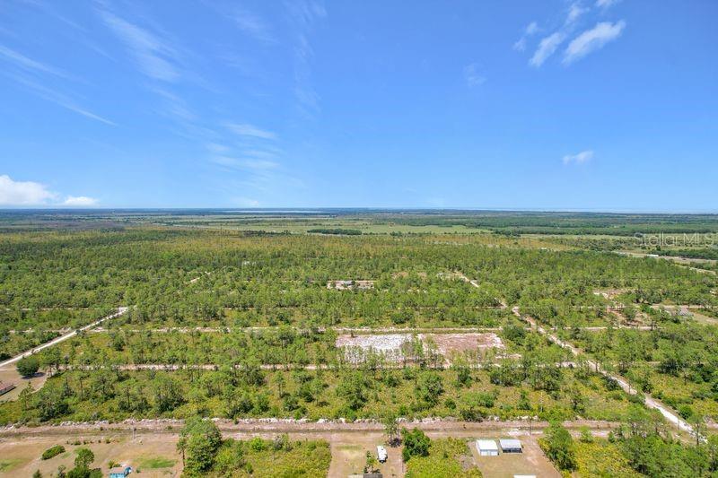 An aerial view shows a vast, flat landscape with scattered trees, dirt roads, and small structures — 0 EL DORADO DRIVE, INDIAN LAKE ESTATES, FL