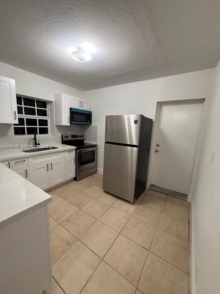 A kitchen features white cabinets, stainless steel appliances, a window, and light-colored tile flooring — 2345 NW 65th St, Miami FL 33147, MIAMI, FL