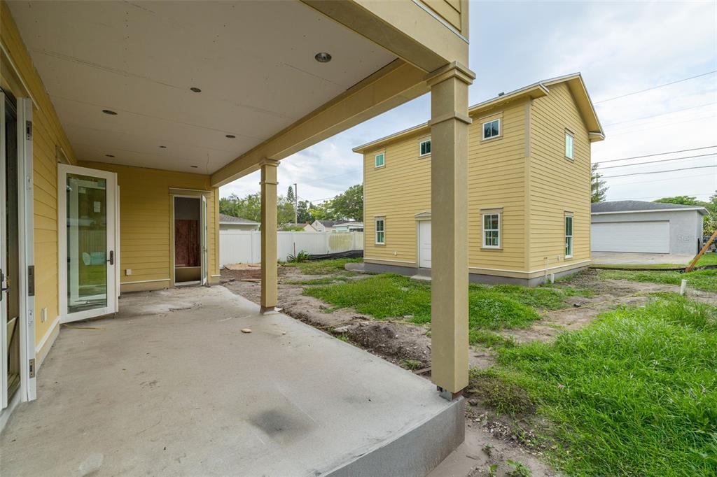 A covered concrete patio overlooks a backyard with a yellow two-story house and detached garage — 3320 15TH STREET N, ST PETERSBURG, FL