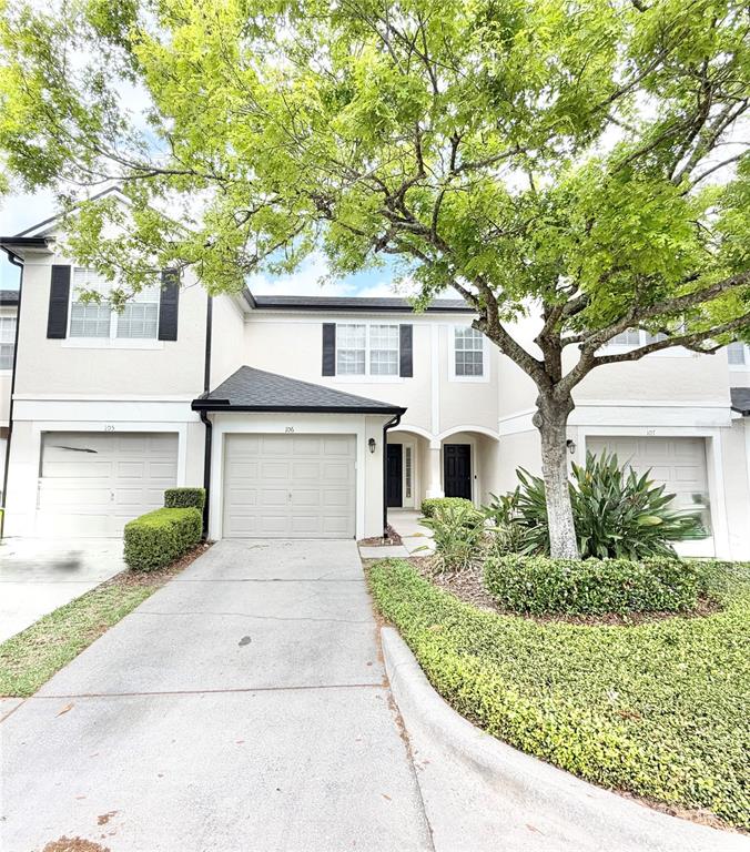 A multi-unit residential building with beige stucco siding, attached garages, and a large shade tree — 6001 TWAIN STREET UNIT 106, ORLANDO, FL