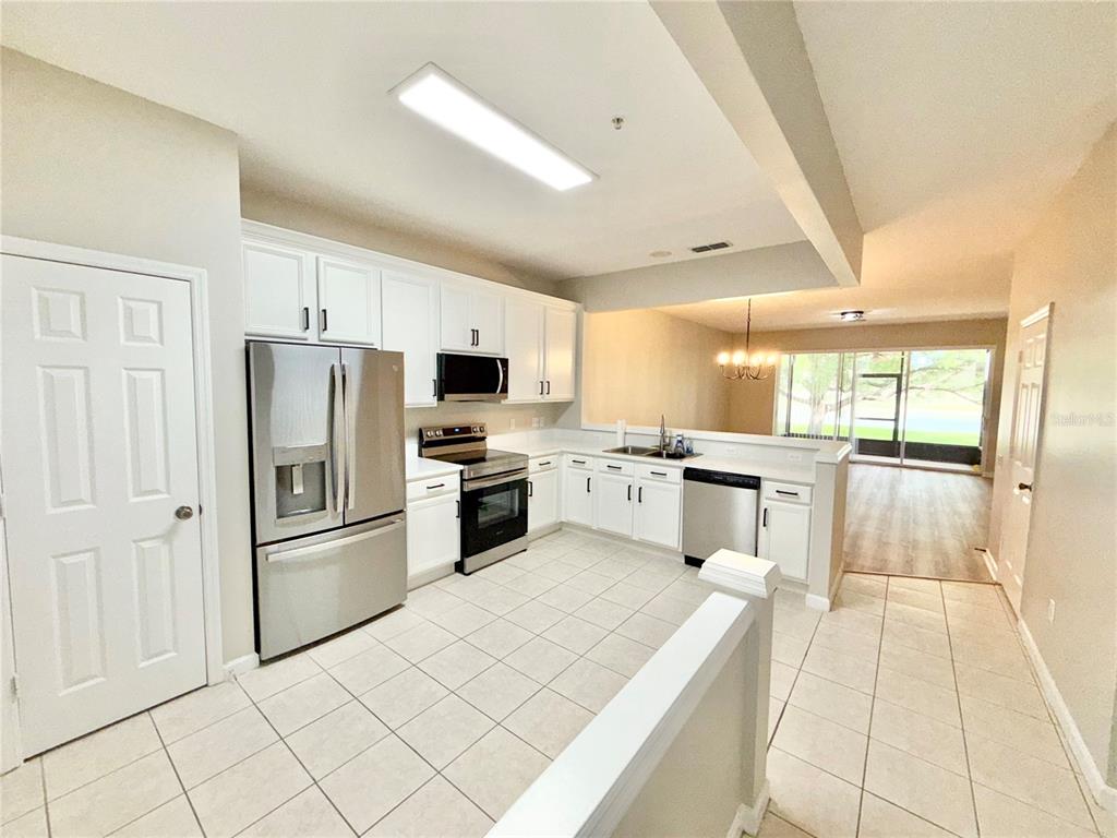 A kitchen with white cabinets, stainless steel appliances, and tile flooring overlooks a living area — 6001 TWAIN STREET UNIT 106, ORLANDO, FL