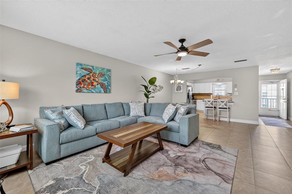A living room with a blue sectional sofa, wooden coffee table, and open kitchen area — 1706 BELLEAIR FOREST DRIVE UNIT 220, BELLEAIR, FL
