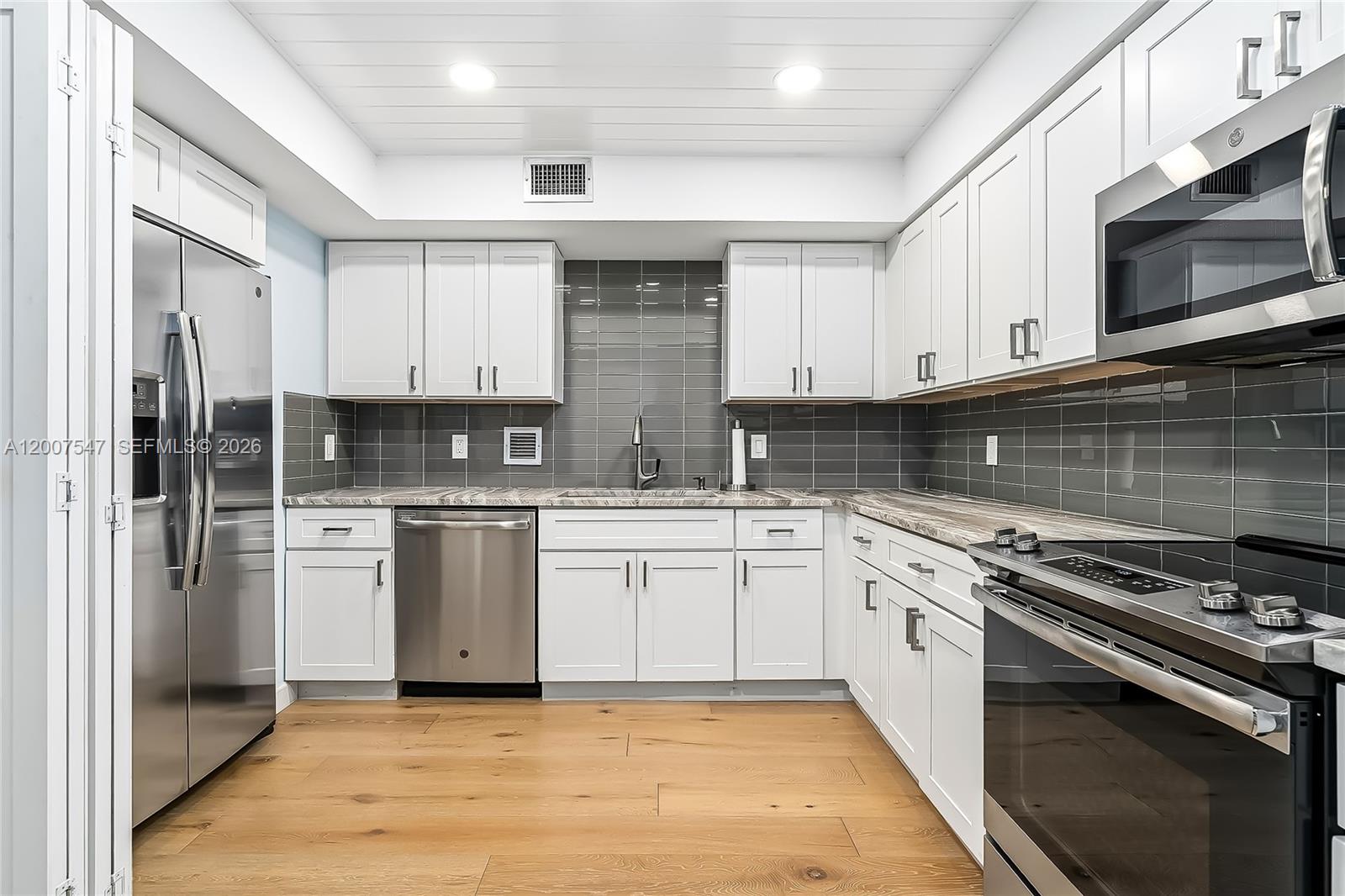 A modern kitchen features white cabinets, stainless steel appliances, gray tile backsplash, and wood flooring — 2808 N 46th Ave # E549, Hollywood FL 33021, HOLLYWOOD, FL