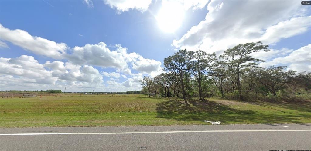 A grassy, vacant lot features a line of trees under a bright, cloudy sky — COMMONWEALTH AVE N, POLK CITY, FL