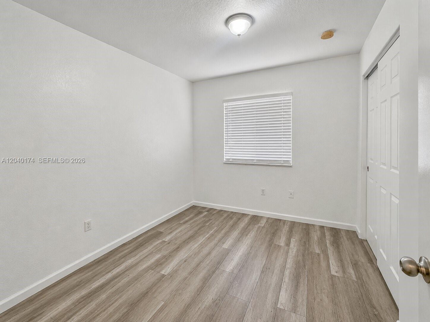 A small, empty bedroom features white walls, wood-look flooring, a window with blinds, and a closet — 31 SE 3, Hallandale Beach FL 33009, HALLANDALE BEACH, FL