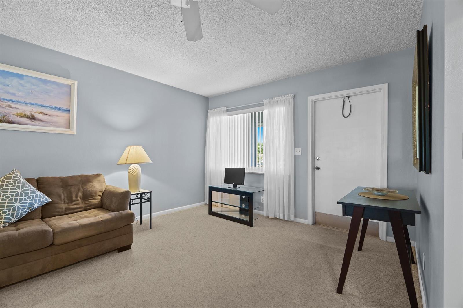 A living room features light blue walls, beige carpeting, a brown sofa, and a desk — 2100 NE 38th Street # 243, Lighthouse Point FL 33064, LIGHTHOUSE POINT, FL