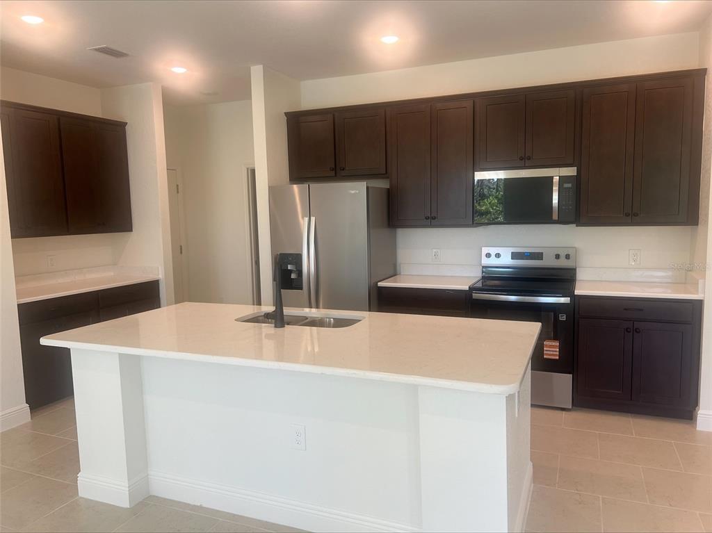 A kitchen features dark wood cabinets, white countertops, stainless steel appliances, and a central island — 1382 SHIELDS STREET, PORT CHARLOTTE, FL