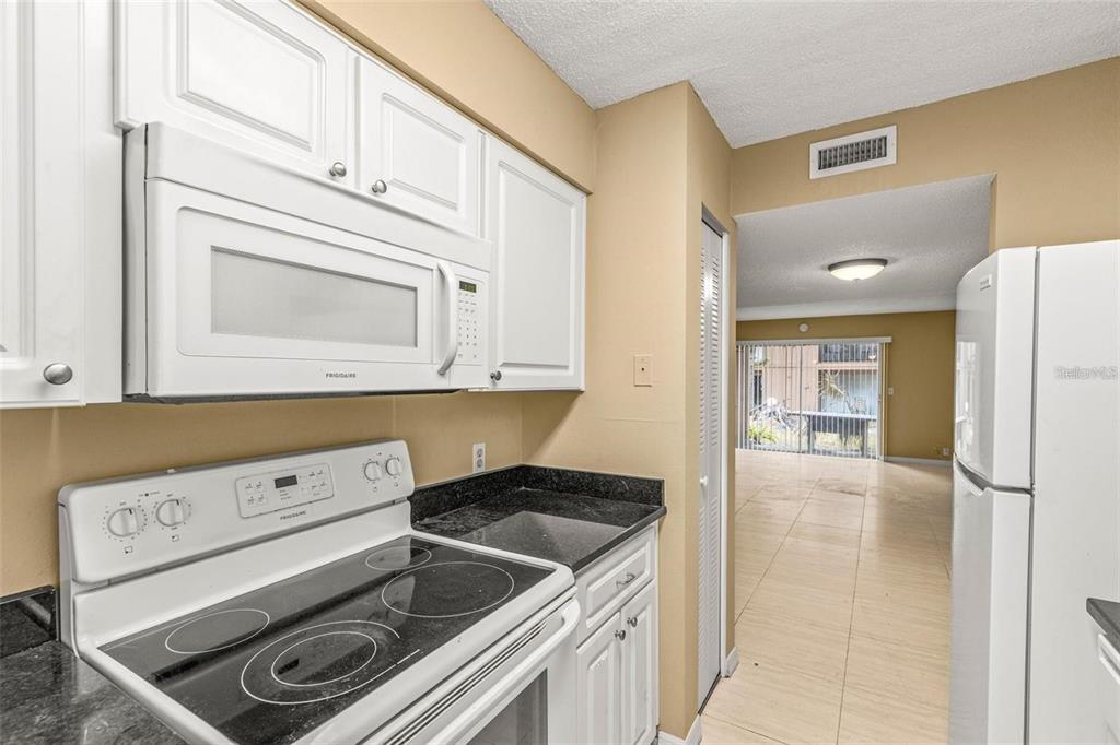 A kitchen with white cabinets, a black countertop, and a white electric stove and microwave — 7510 PRESLEY PLACE UNIT 98-A, TAMPA, FL
