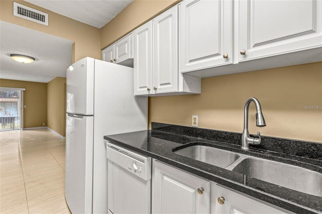 A kitchen features white cabinets, black granite countertops, a stainless steel sink, and white appliances — 7510 PRESLEY PLACE UNIT 98-A, TAMPA, FL