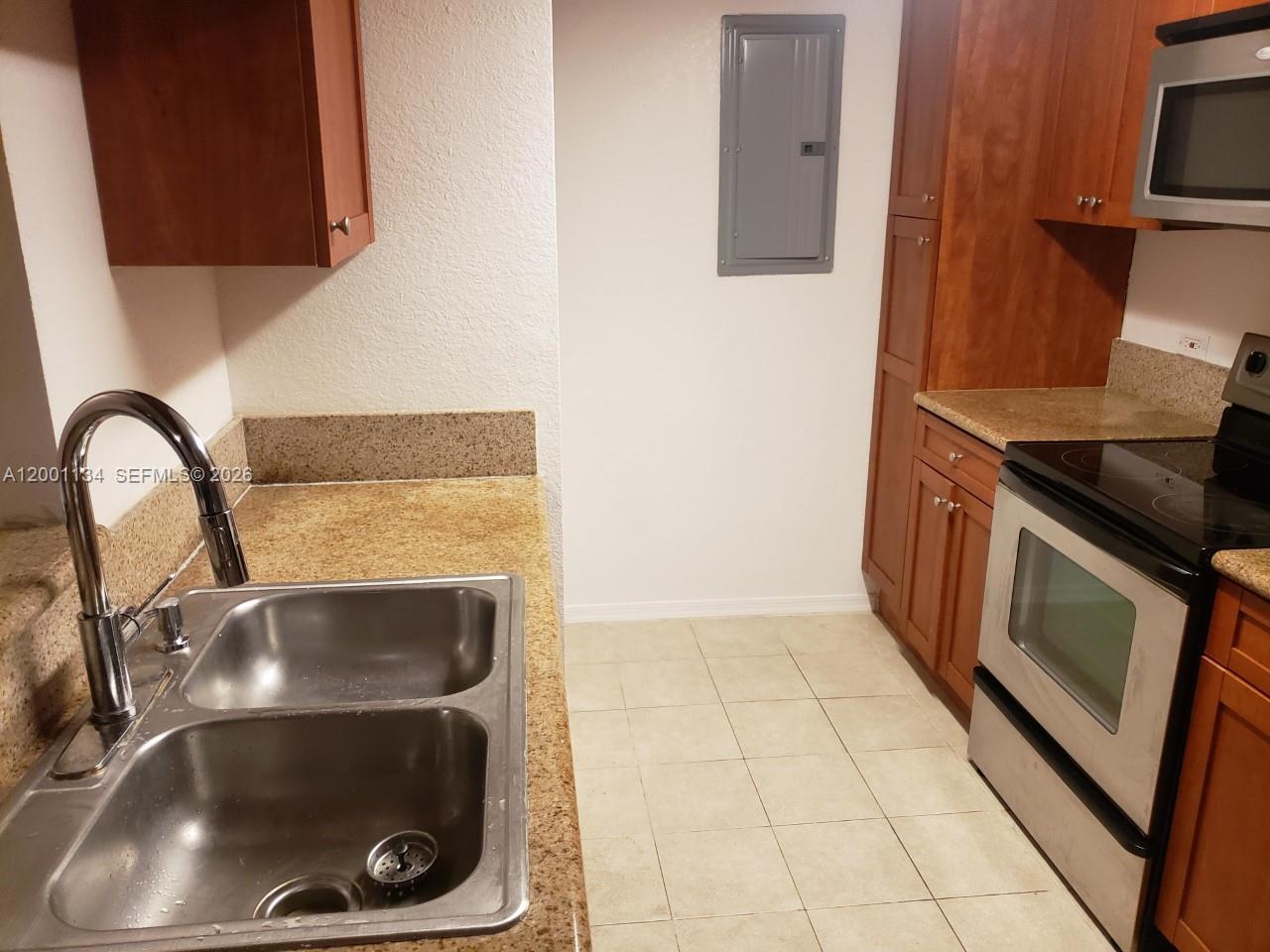 A kitchen features a double-basin stainless steel sink, wood cabinets, and a black electric stove — 36 NW 6th Ave # 906, Miami FL 33128, MIAMI, FL