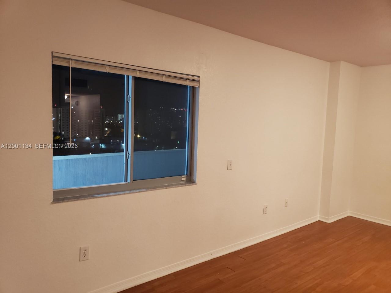 An empty room features white walls, wood-look flooring, and a window overlooking a city at night — 36 NW 6th Ave # 906, Miami FL 33128, MIAMI, FL