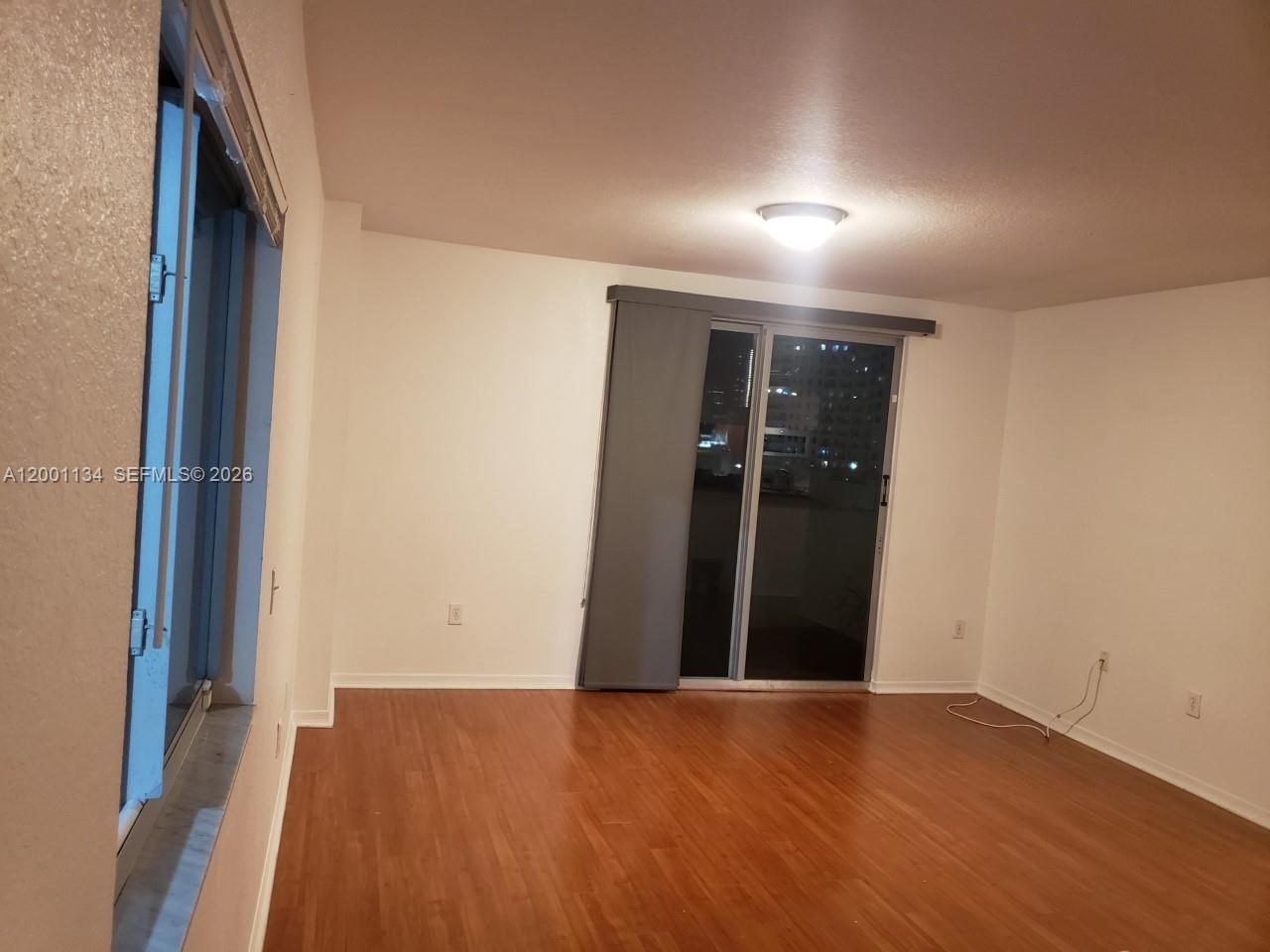 An empty room features wood-look flooring, a sliding glass door, and a large window — 36 NW 6th Ave # 906, Miami FL 33128, MIAMI, FL
