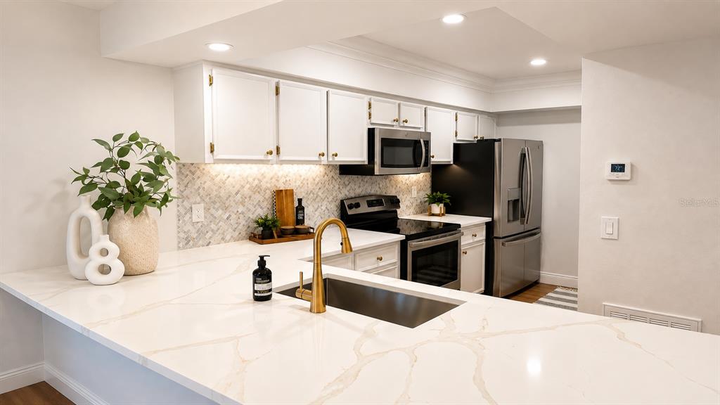 A modern kitchen features white cabinets, marble-patterned countertops, a gold faucet, and stainless steel appliances — 2981 BONAVENTURE CIRCLE UNIT 202, PALM HARBOR, FL