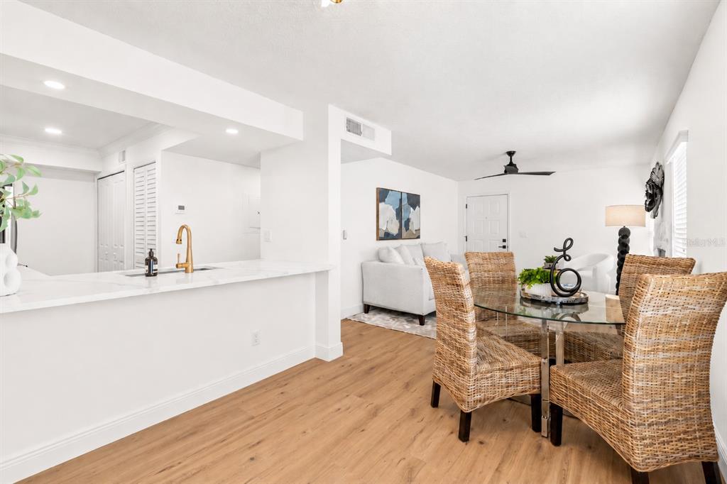 A dining area with a glass table and wicker chairs sits beside a white kitchen counter — 2981 BONAVENTURE CIRCLE UNIT 202, PALM HARBOR, FL