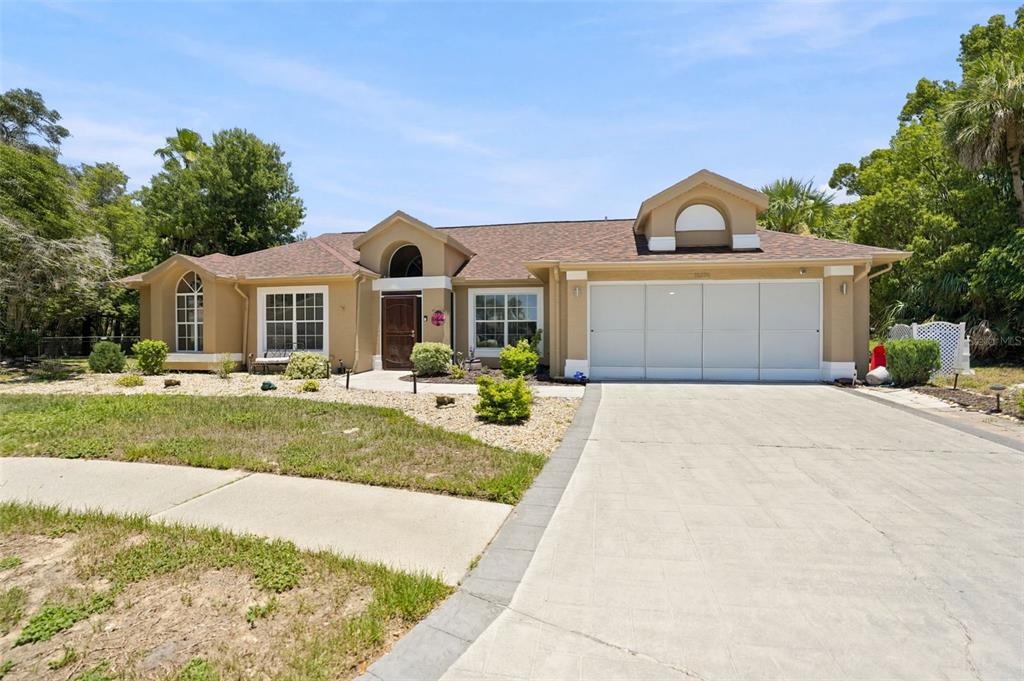 A single-story tan house with a three-car garage and a paved driveway — 10296 WINDSOR COURT, SPRING HILL, FL