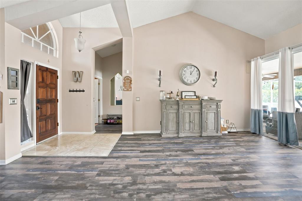 A living room features wood-look plank flooring, a wooden front door, and a large wall clock — 10296 WINDSOR COURT, SPRING HILL, FL