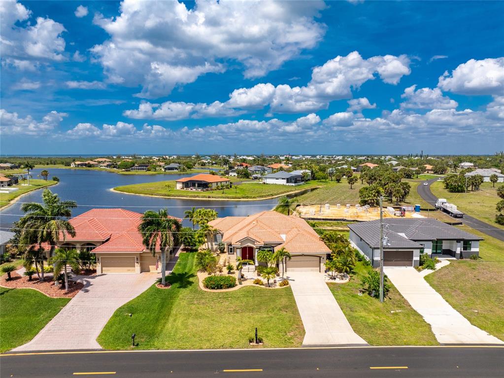 An aerial view shows three suburban houses with driveways facing a road and a lake — 16237 CAPE HORN BOULEVARD, PUNTA GORDA, FL