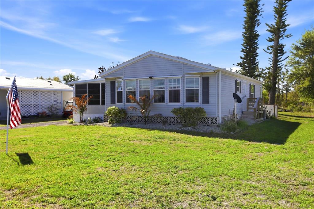A light blue manufactured home with a screened porch and an American flag in the yard — 29215 EDGEWOOD STREET, PUNTA GORDA, FL