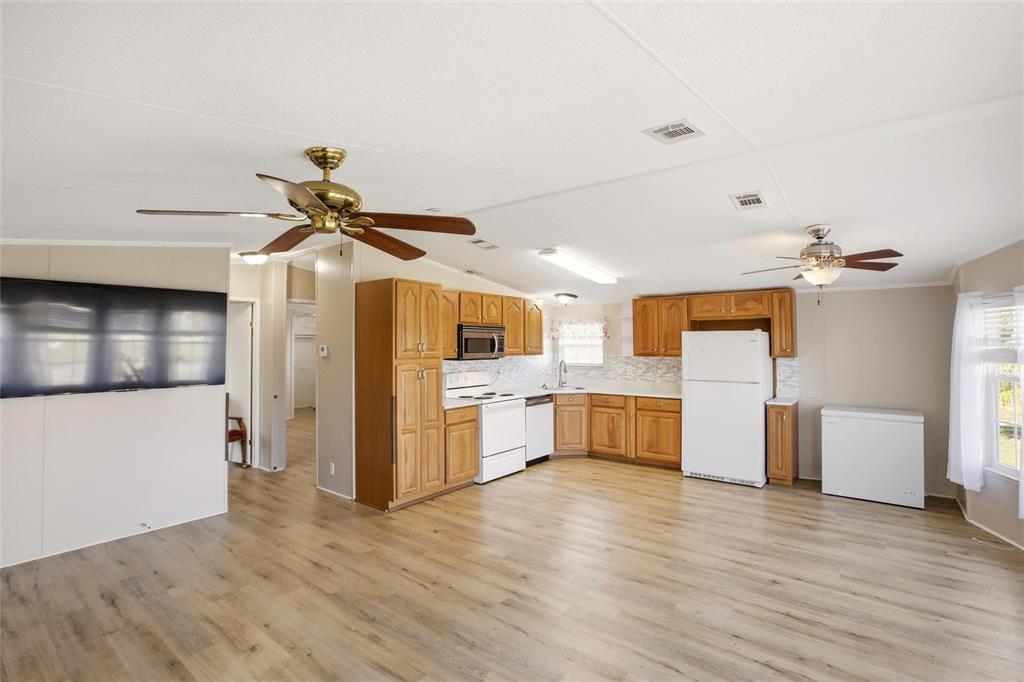 An open-concept kitchen and living area features wood cabinets, white appliances, and light wood flooring — 29215 EDGEWOOD STREET, PUNTA GORDA, FL