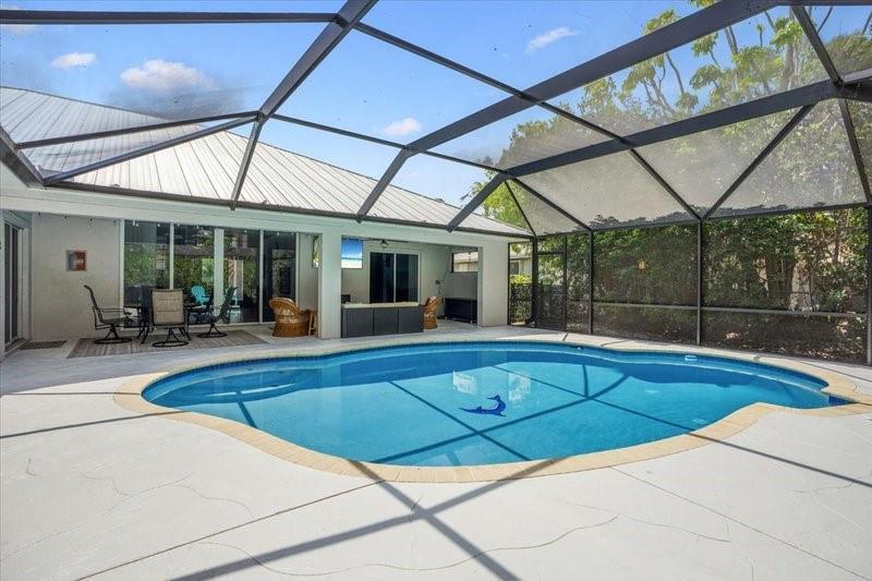 A screened-in swimming pool sits on a patio adjacent to a house with outdoor seating — PORT ST. LUCIE, FL