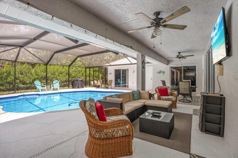 A covered patio features a swimming pool, outdoor seating, a ceiling fan, and a wall-mounted television — PORT ST. LUCIE, FL