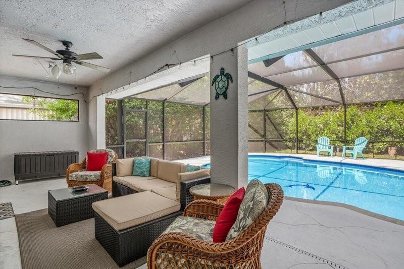 A covered patio features wicker furniture, a ceiling fan, and a screened-in swimming pool — PORT ST. LUCIE, FL