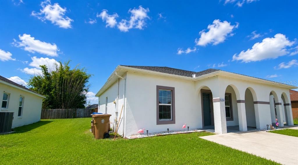 A white single-story house with arched entryways sits on a green lawn under a blue sky — 828 ABBEVILLE COURT, KISSIMMEE, FL