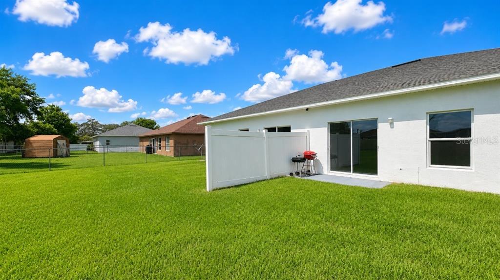 The backyard features a white vinyl privacy fence, a small grill, and a sliding glass door — 828 ABBEVILLE COURT, KISSIMMEE, FL