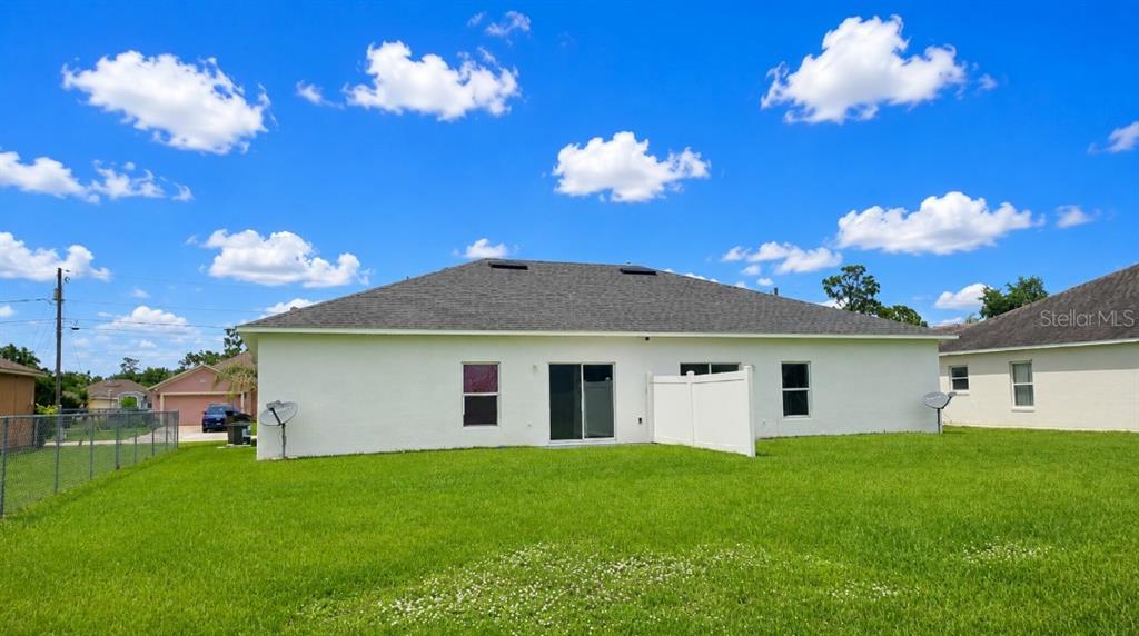The back exterior of a white house features a gray roof and a grassy yard — 828 ABBEVILLE COURT, KISSIMMEE, FL