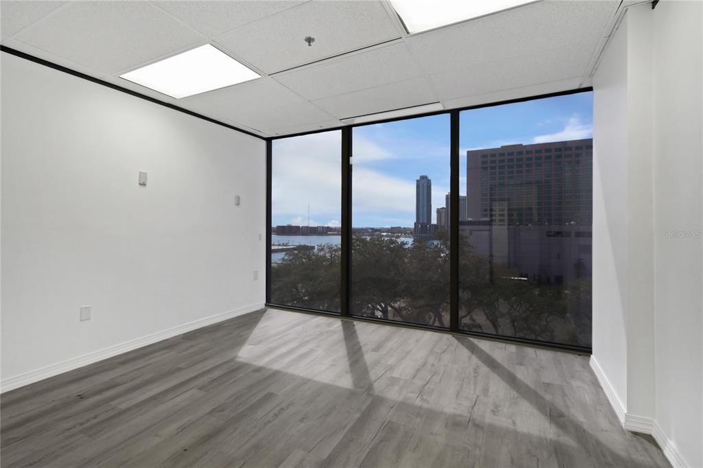 An empty office space features gray wood-look flooring, white walls, and floor-to-ceiling windows with city views — 233 E BAY STREET UNIT 606, JACKSONVILLE, FL