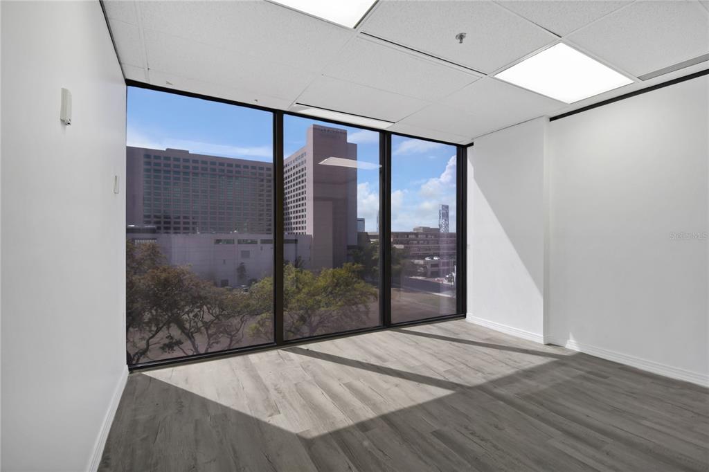 An empty office with light wood-look flooring and large windows overlooking a city skyline — 233 E BAY STREET UNIT 606, JACKSONVILLE, FL