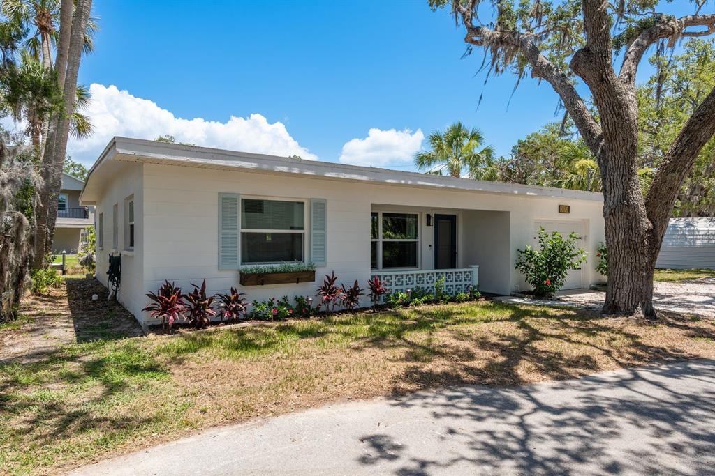 A white single-story house with blue shutters, a front porch, and a large oak tree — 5270 MILLER BAYOU DRIVE, PORT RICHEY, FL