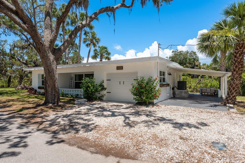A white single-story house with a gravel driveway, a carport, and large oak trees — 5270 MILLER BAYOU DRIVE, PORT RICHEY, FL