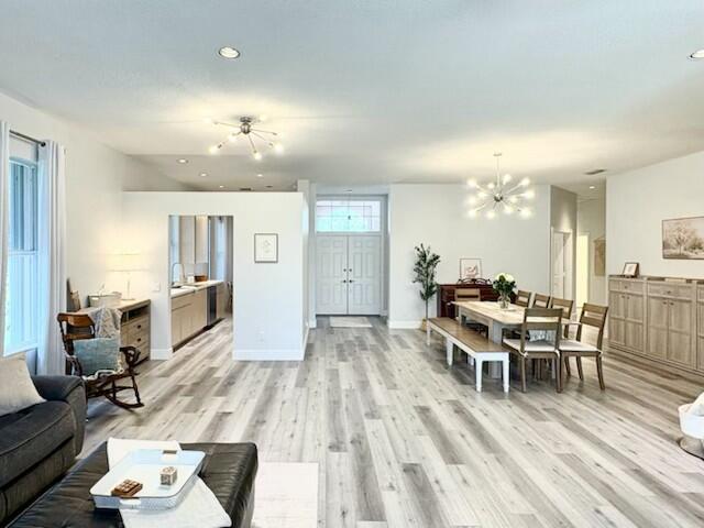 An open-concept living and dining area features light wood-look flooring and modern light fixtures — 5018 SE Heartleaf Terrace, Hobe Sound FL 33455, HOBE SOUND, FL