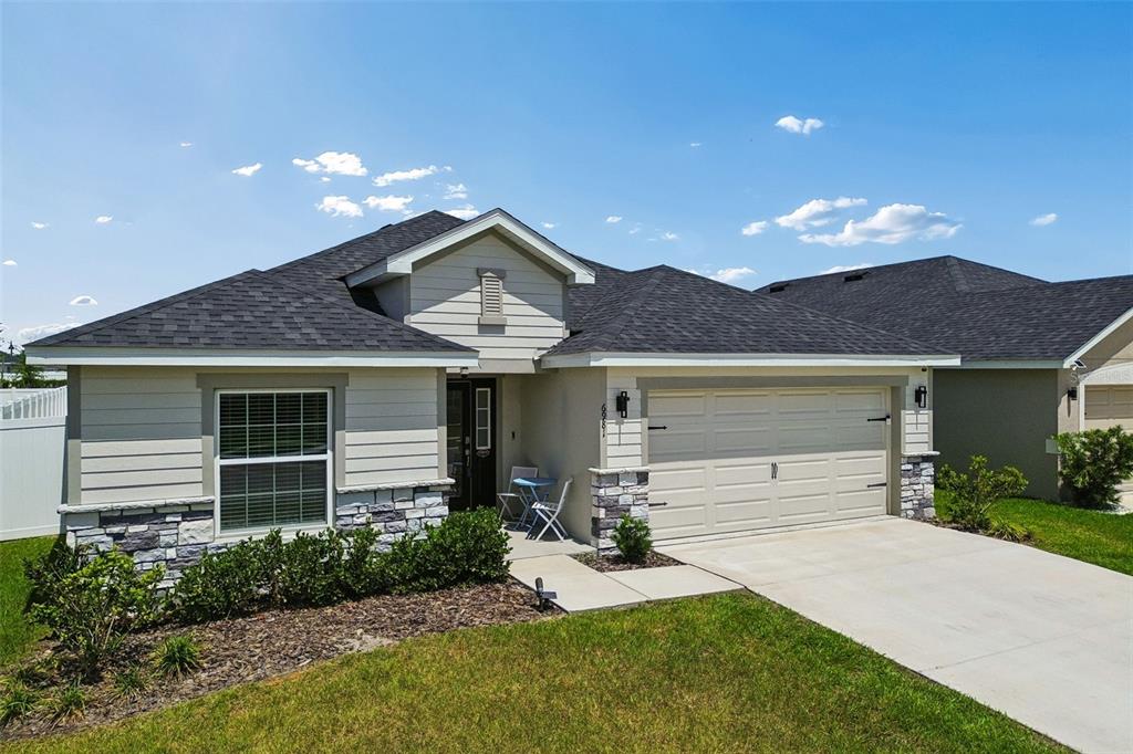 A single-story house with a beige exterior, stone accents, and a two-car garage — 6981 TWISTING PINES LOOP, ZEPHYRHILLS, FL