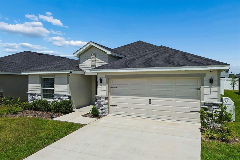 A single-story house features a two-car garage, stone accents, and a beige stucco exterior — 6981 TWISTING PINES LOOP, ZEPHYRHILLS, FL