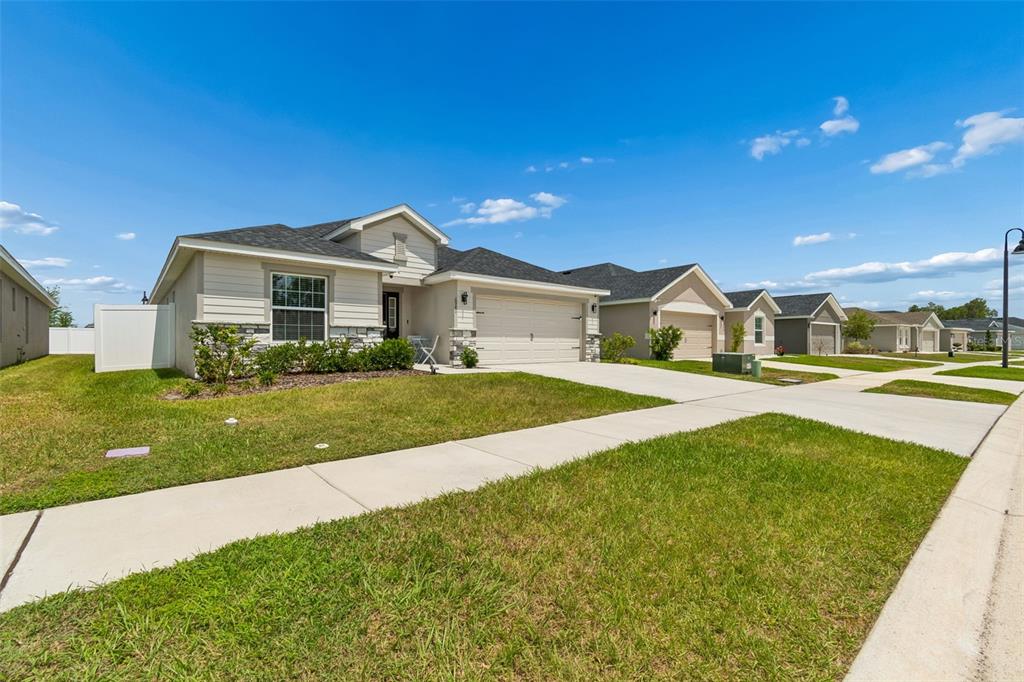 A single-story suburban house with beige siding, a stone facade, and a two-car garage — 6981 TWISTING PINES LOOP, ZEPHYRHILLS, FL