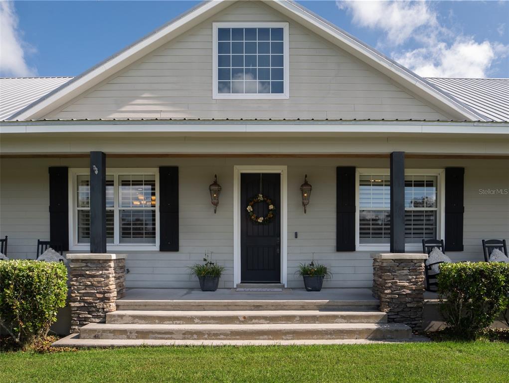 A light gray house features a covered front porch with stone pillars and black shutters — 13211 NW 115TH STREET, OCALA, FL