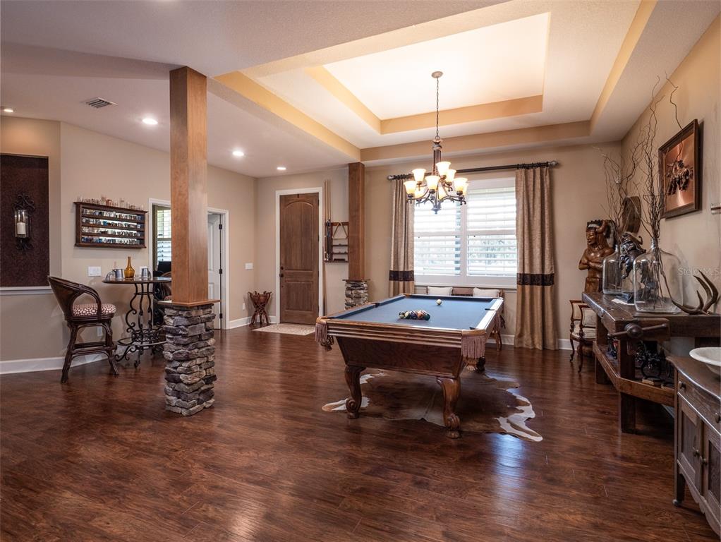 A game room features a pool table, hardwood floors, stone-accented columns, and a tray ceiling — 13211 NW 115TH STREET, OCALA, FL