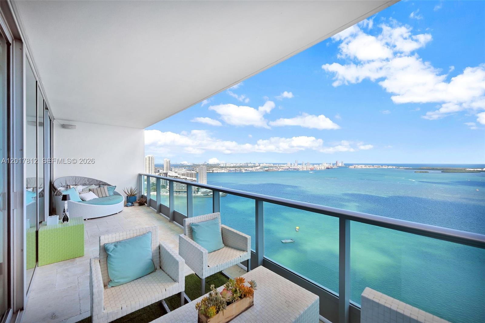 A high-rise balcony features outdoor furniture overlooking a bay with a distant city skyline — 1331 Brickell Bay Dr # 3607, Miami FL 33131, MIAMI, FL