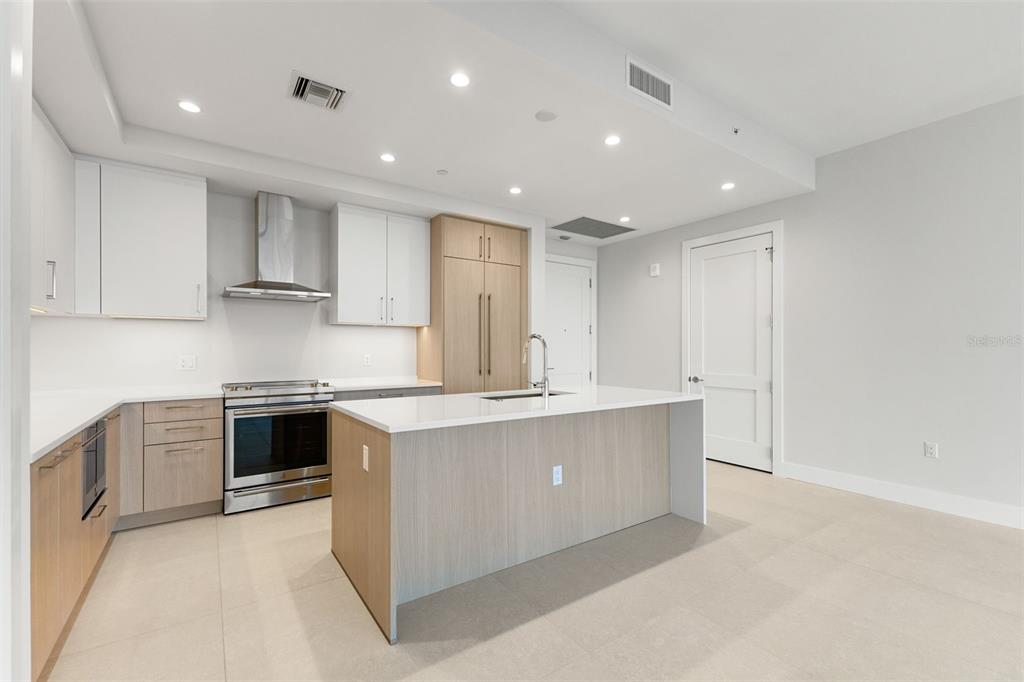 A modern kitchen features white upper cabinets, light wood lower cabinets, and a central island — 275 1ST AVENUE S UNIT 2308, ST PETERSBURG, FL
